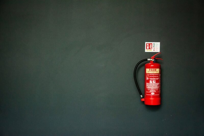 A wall-mounted fire extinguisher with a fire extinguisher sign above it on a black wall in a dentist.